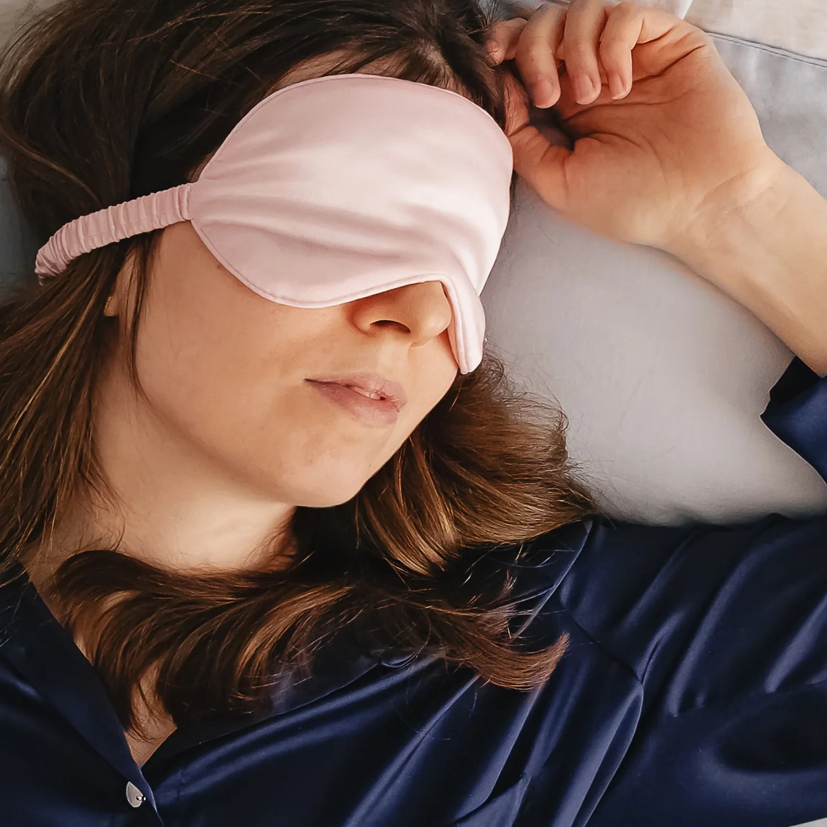 femme allongée portant un masque de sommeil en soie rose poudré Scrunch'it Silk