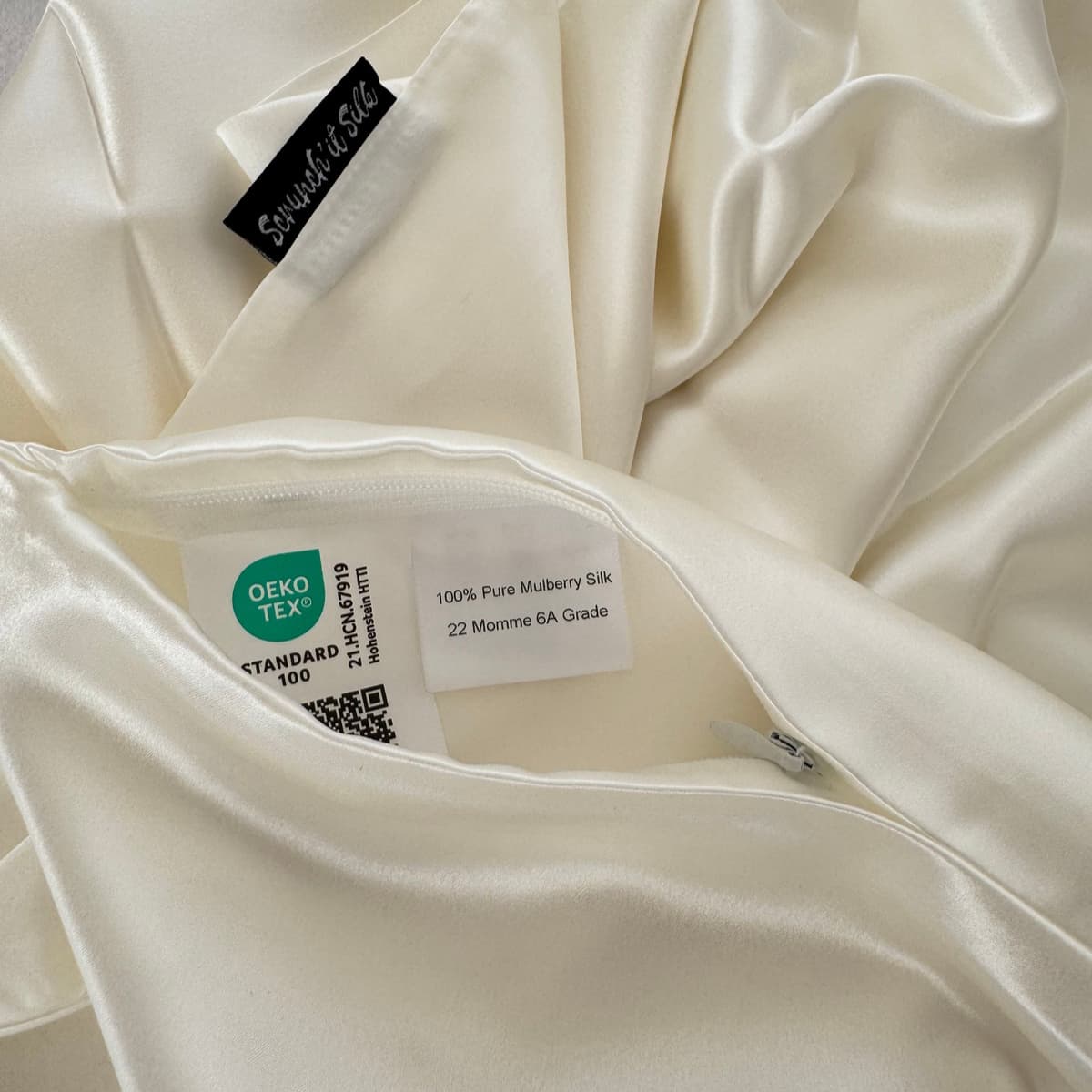 Détail de la taie d'oreiller en soie ivoire Scrunch'it Silk, avec fermeture éclair et étiquettes 22 mommes Grade 6A et OEKO-TEX Standard 100.