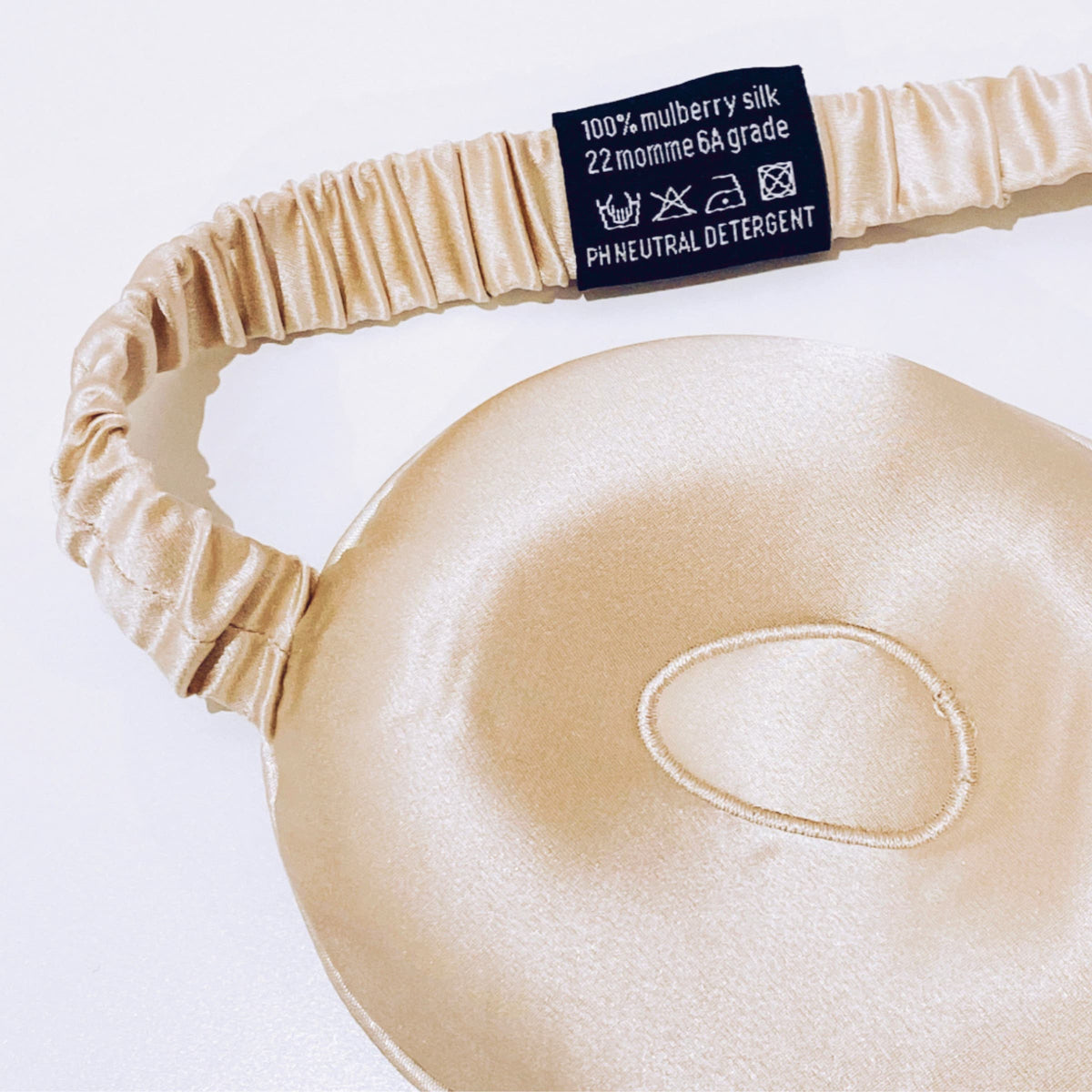 Gros plan de l'intérieur du masque de sommeil contour champagne en soie de mûrier 22 mommes, avec bande élastique et étiquette d'entretien - Scrrunch'it Silk.