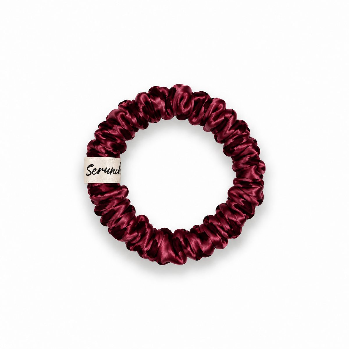 Chouchou fin en soie Scrunch'it Silk bordeaux, avec étiquette crème de la marque, sur fond blanc.