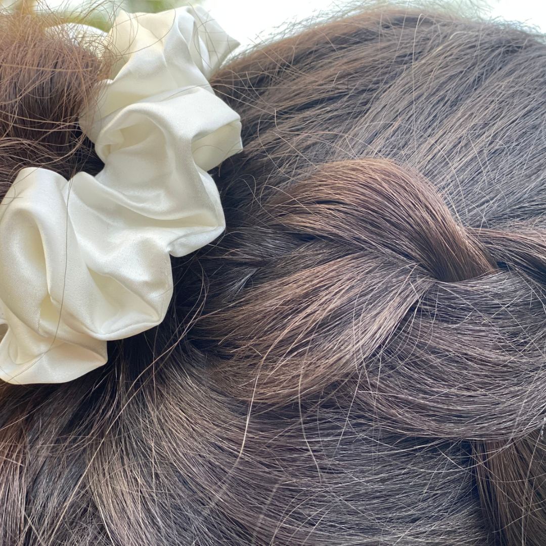 Gros plan d'une tresse brune attachée avec un chouchou en soie large Scrunch'it Silk couleur ivoire.