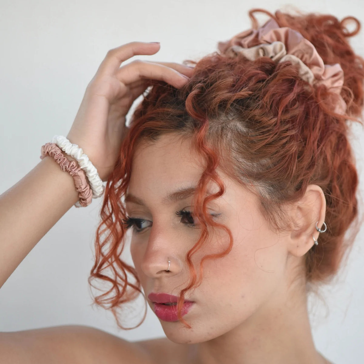 L'influenceuse Tafukt aux cheveux bouclés attachés avec deux chouchous en soie larges saumon et beige et deux chouchous fin saumon et ivoire Scrunch'it Silk au poignet.